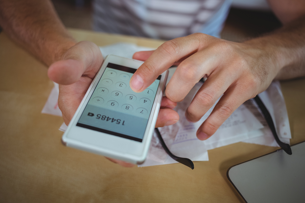 Mid section of man calculating bills on mobile phone-1